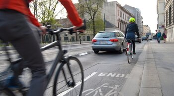 Fahrrad- und Autofahrer bewegen sich auf einer Straße fort.