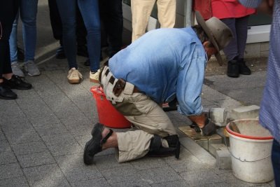 Der Künstler Gunter Demnig kniet am Boden und verlegt die goldenen "Stolpersteine".